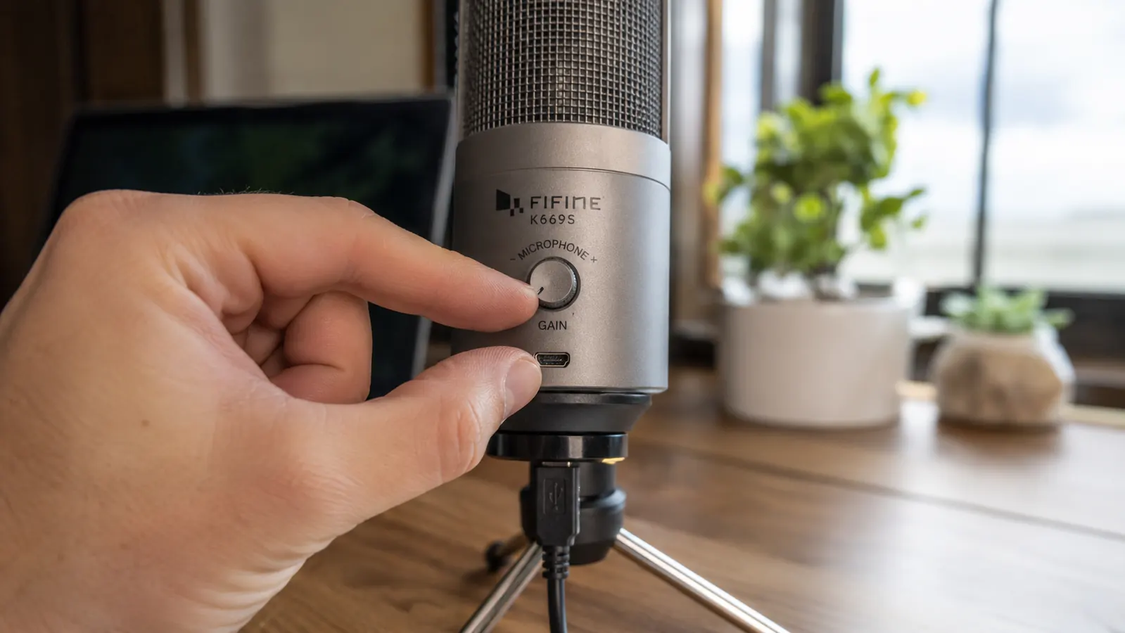 Hand adjusting the gain control knob on the back of a silver USB desktop microphone