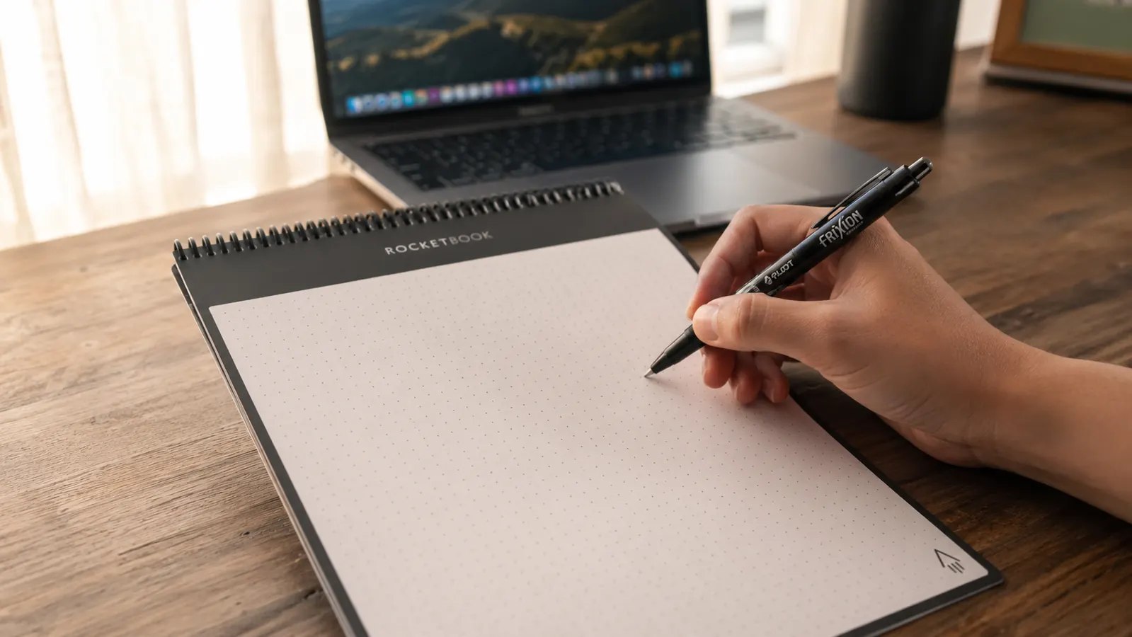 Hand writing in a black Rocketbook Flip notepad open on a tidy home office desk