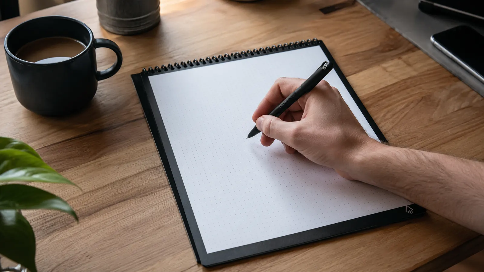 Hand writing meeting notes in a Rocketbook Flip notebook with the included pen at a desk
