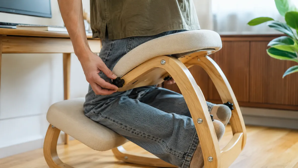 Hand adjusting the seat angle lever on the frame of a black kneeling chair before sitting down