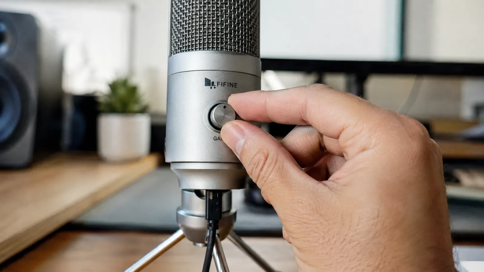Hand adjusting the gain dial on the body of a silver metal USB desktop microphone
