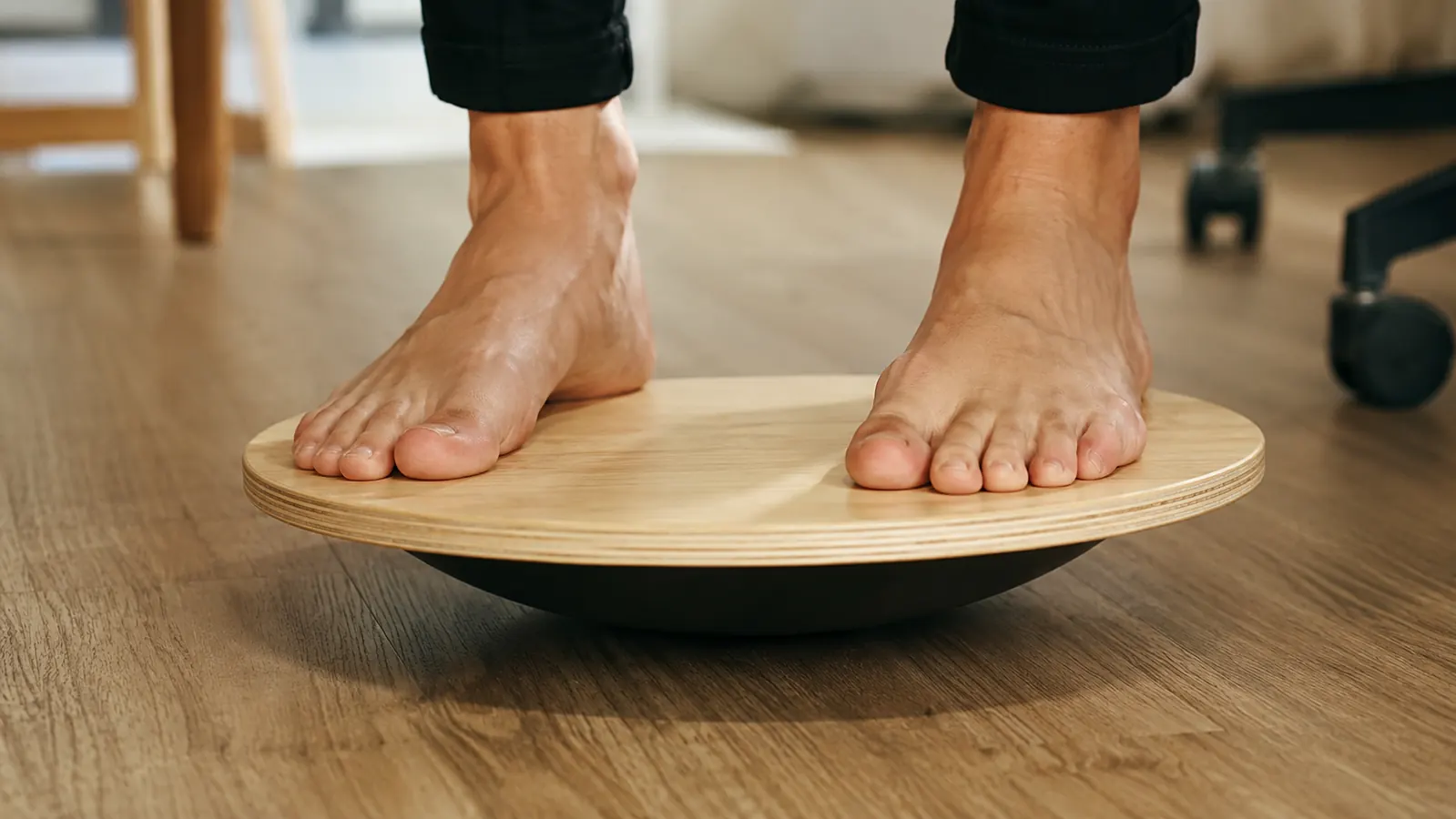 Close-up of bare feet balanced on the wobble side of a round wooden balance board on a home office floor