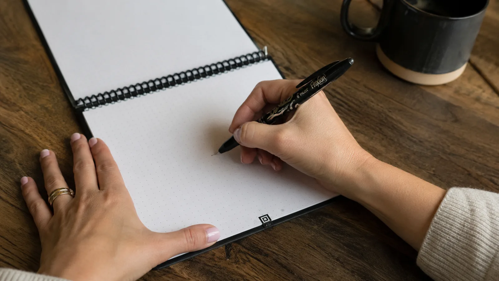 Hand writing in the Rocketbook Flip with a Pilot FriXion pen at a desk