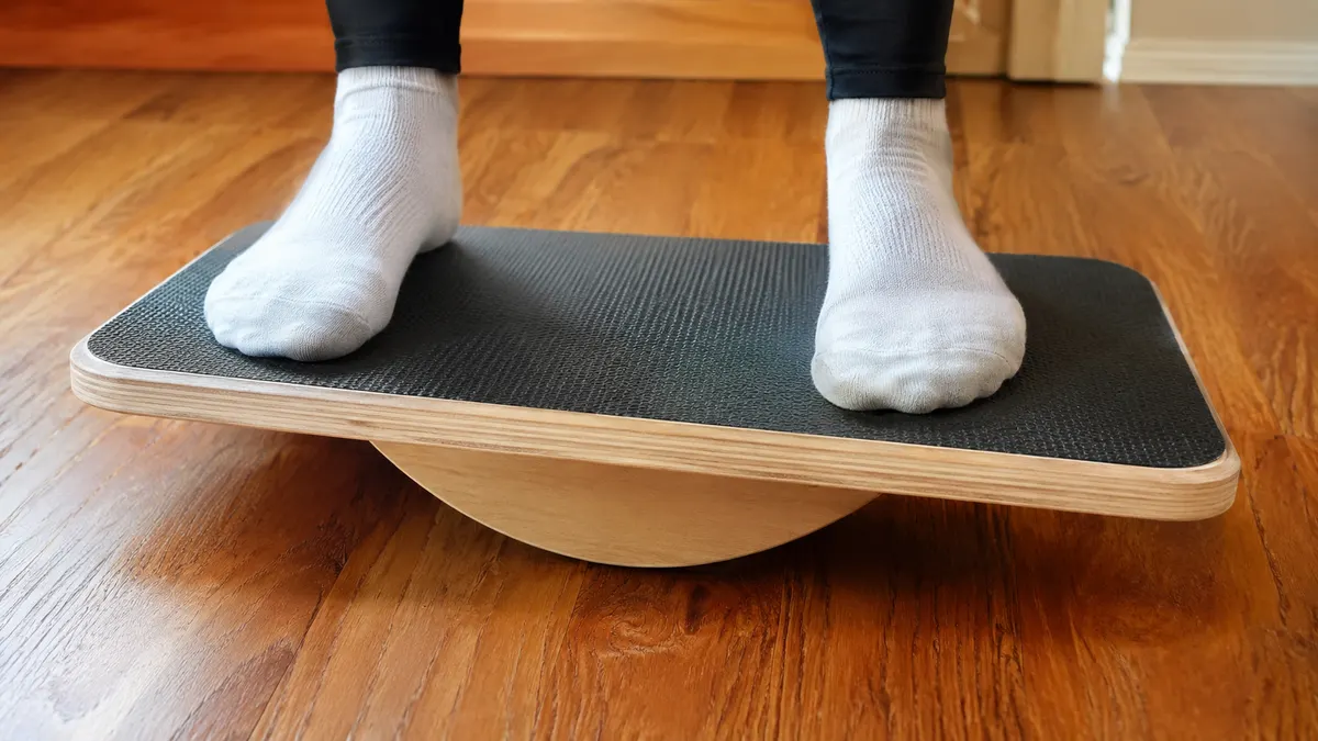 Close-up of bare feet balanced on the ridged wooden balance board on a hardwood floor